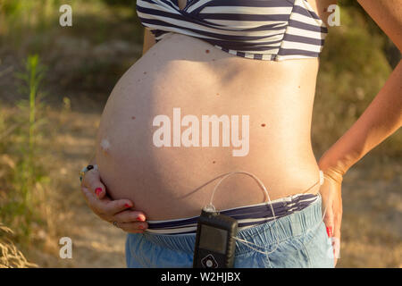 Un diabetico donna incinta con una pompa di insulina in una foresta. Sta indossando un mantello blu e un striped bikini top. Foto Stock