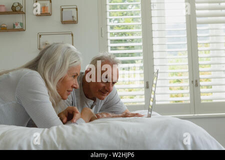 Attivo coppia senior utilizzando laptop mentre giaceva sul letto in camera da letto Foto Stock