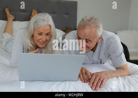 Attivo coppia senior utilizzando laptop mentre giaceva sul letto in camera da letto Foto Stock