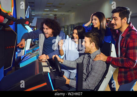 Un gruppo di amici a giocare macchina arcade. in un parco di divertimenti. I giovani hanno il divertimento. Foto Stock