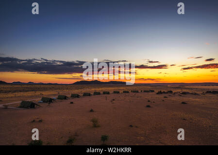 Il tramonto sopra i piccoli chalets di una desert lodge vicino al Sossusvlei in Namibia Foto Stock