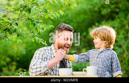 Figlio di alimentazione solidi. Il tuo bimbo. Nutrizione naturale concetto. Papà e carino toddler boy avente il pranzo all'aperto. Prodotti per la cura del bambino. Figlio di alimentazione alimenti naturali. Feed in modo giusto per bambini nello stadio di sviluppo. Foto Stock