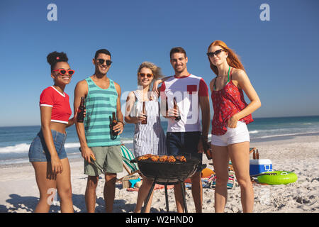 Gruppo di amici divertendosi durante la preparazione di cibo sul barbecue in spiaggia Foto Stock