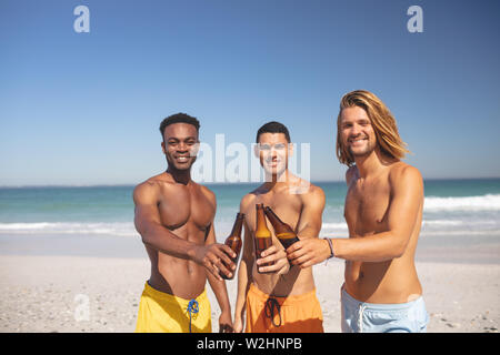 Amici maschi tostare le bottiglie di birra sulla spiaggia Foto Stock