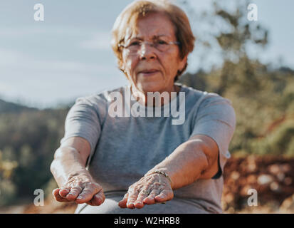 Donna anziana facendo loro si estende nel parco con il fuoco selettivo nelle dita Foto Stock