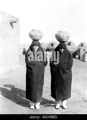 Due femmine, a lunghezza piena, indossando coperte, pentole su capi Foto Stock