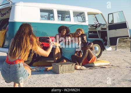 Donna di fotografare i suoi amici con il telefono cellulare vicino a camper van a beach Foto Stock