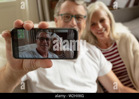 Active senior giovane seduto sul divano e prendendo selfie in una casa confortevole Foto Stock