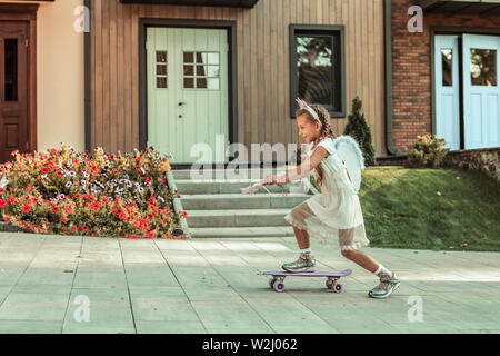 Attività sportive giovane ragazza in abito bianco attivamente a cavallo su uno skateboard Foto Stock