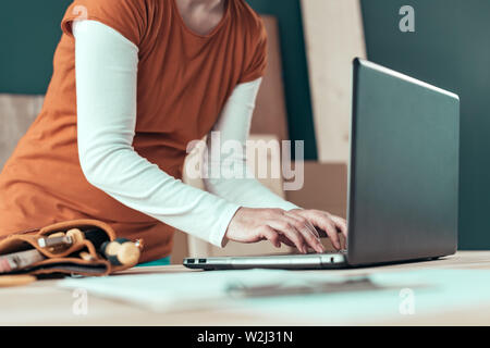 Falegname femmina digitando computer portatile tastiera in laboratorio di falegnameria Foto Stock