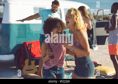 Gruppo di amici divertendosi vicino a camper van a beach Foto Stock