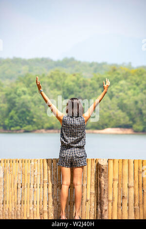 Donne alzando le braccia e sullo sfondo le montagne e acqua al serbatoio Chakrabongse , Prachinburi in Thailandia. Foto Stock