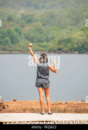 Donne alzando le braccia e sullo sfondo le montagne e acqua al serbatoio Chakrabongse , Prachinburi in Thailandia. Foto Stock