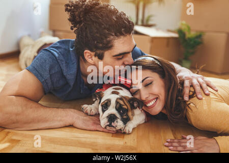 La giovane coppia felice si trasferisce in una nuova casa. Sono sdraiato sul pavimento con il loro piccolo cucciolo dopo che avevano portato a caselle con cose da th Foto Stock