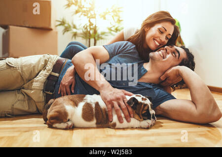 La giovane coppia felice si trasferisce in una nuova casa. Sono sdraiato sul pavimento con il loro piccolo cucciolo dopo che avevano portato a caselle con cose da th Foto Stock