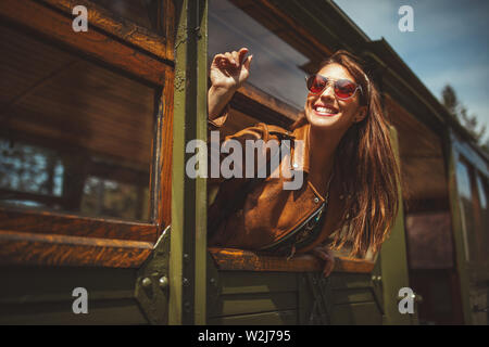 Una giovane e bella donna è guardando attraverso un treno di retrò finestra e oscilla a qualcuno, durante il suo viaggio verso un'avventura. Foto Stock