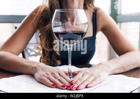Bevuto donna seduta al tavolo e con in mano un bicchiere di vino di close-up. Alcolismo femminile. Foto Stock