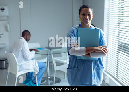 Medico donna file di contenimento e sorridente in ospedale Foto Stock