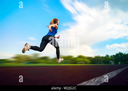 La giovane ragazza in esecuzione in Stadium, la sfocatura in movimento. Un atleta che corre intorno allo stadio jumping foto in volo. Atletica leggera Foto Stock