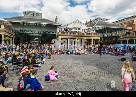 Un esecutore di strada intrattiene la folla di turisti al mercato di Covent Garden, Londra Foto Stock