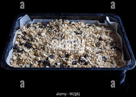 Granola in un nero vassoio da forno con la carta pergamena pronto per essere cotto al forno da lato Foto Stock