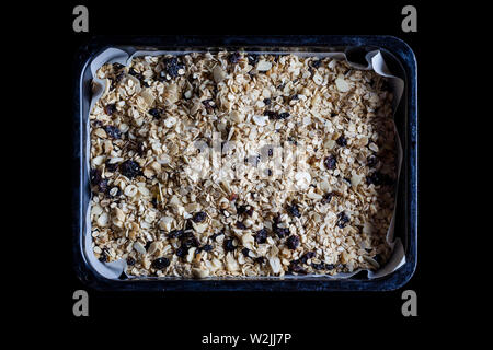Granola in un nero vassoio da forno con la carta pergamena pronti per essere cotti direttamente dal di sopra Foto Stock