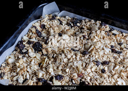 Granola in un nero vassoio da forno con la carta pergamena pronto per essere cotto al forno da lato closeup Foto Stock