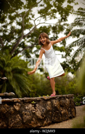 Sorridente ragazza divertirsi bilanciamento sulla parete di pietra di un giardino si trova un laghetto artificiale. Foto Stock