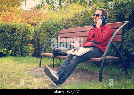 Difficile conversazione aziendale sul telefono, risolvere i problemi sul posto di lavoro. insoddisfatto uomo che lavora sul computer portatile. Parlando sullo smartphone, in seduta Foto Stock