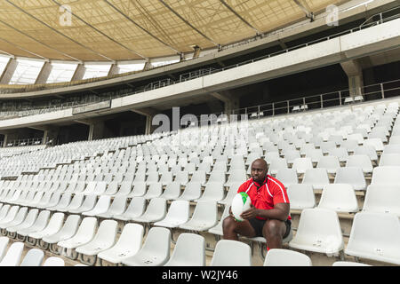 Sconvolto americano africano rugby maschio giocatore seduto con palla da rugby in stadium Foto Stock