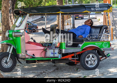 Bangkok, Tailandia - 14 Aprile 2019: Taxi driver dormire nel suo tuk tuk parcheggiato nei pressi della strada Foto Stock