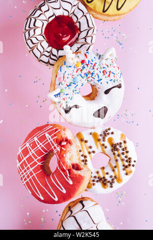 Varie ciambelle decorate in movimento che rientrano su sfondo rosa. Dolce e colorata ciambelle battenti in movimento. Foto Stock