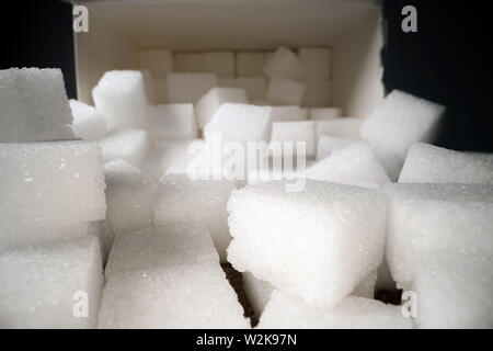 Macro shot di cubetti di zucchero accanto alla scatola di cartone sul tavolo di legno. Cibo malsano dolcificante, dolci cubetti di cristallo Foto Stock