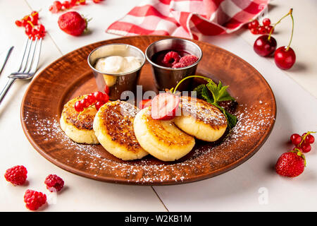 Cottage cheese pancakes, fatti in casa tradizionale piatto ucraino syrniki con salsa di frutti di bosco e panna acida su una piastra marrone su sfondo bianco Foto Stock