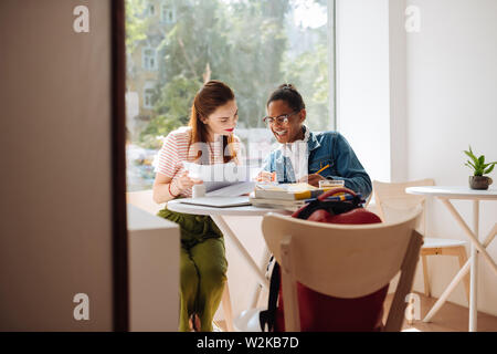 L'atmosfera cordiale. Carino brunette ragazza con fogli di carta durante la verifica del compito a casa Foto Stock