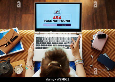 Vista superiore della infelice donna moderna seduti sul divano del soggiorno moderno avente 404 Pagina non trovata errore su un computer portatile. Foto Stock