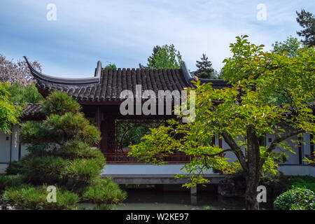 Tetto di un tradizionale edificio Cinese, circondato da vegetazione su una chiara giornata di sole a Dr. Sun Yat-Sen classico giardino Cinese in Vancouver BC Foto Stock