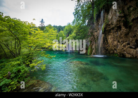 Le acque di un piccolo torrente precipita la roccia nell'azzurro acqua colorata di un laghetto al Parco Nazionale dei Laghi di Plitvice in Croazia Foto Stock
