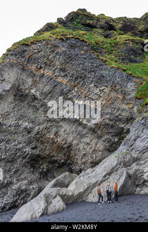 I visitatori di sostare sotto una sezione di colonne di basalto Reynisfjara sulla spiaggia di sabbia nera, sud dell'Islanda. Foto Stock