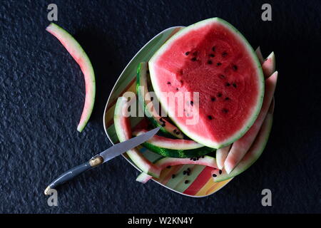 Pezzo di anguria rosso con tagliare a fette e mangiato su una piastra con un coltello su un sfondo nero Foto Stock