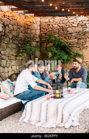 Ritratto di felice giovani seduti insieme e ridere mentre godendo di un partito di cocktail sul tavolo. Foto Stock