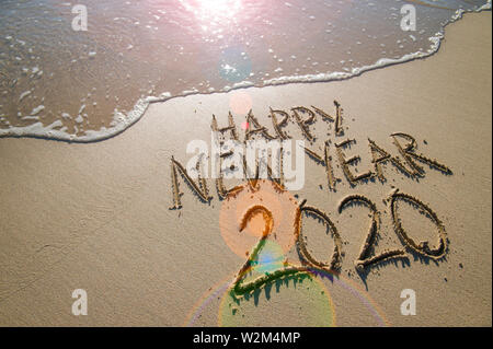 Felice Anno Nuovo 2020 messaggio scritto a mano sollevata in lettere a trama su una spiaggia di sabbia con buon spazio copia accanto a onda che sopraggiungono Foto Stock