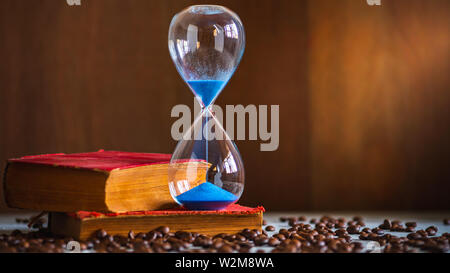 Orologio di sabbia sul vecchio libro e semi di caffè sul tavolo di legno. Copia spazio per il testo. Il concetto di tempo per leggere i libri. Foto Stock