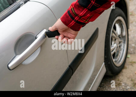 L uomo si apre meccanicamente la sua auto inserendo la chiave. Girando la chiave nella toppa di chiave sulla maniglia della porta di un veicolo parcheggiato. Con la mano destra che con la mano la persona intende apertura Foto Stock