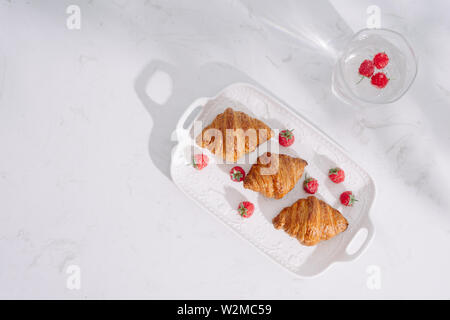 Croissant con lamponi. I lamponi con croissant. Croissant su uno sfondo luminoso con bacche di lampone Foto Stock