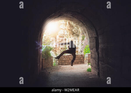 Silhouette di un uomo salta durante la pratica del karate si muove in un buio del tunnel Foto Stock