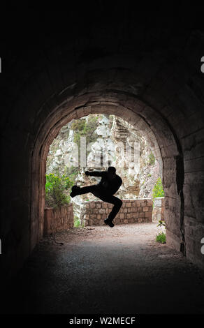 Silhouette di un uomo a praticare il karate si muove in un buio del tunnel Foto Stock