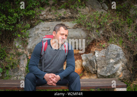 Maschio caucasico con uno zaino pausa di riposo su una panchina mentre si cammina su un percorso in un bosco su un sentiero costiero a Petrovac, Montenegro Foto Stock