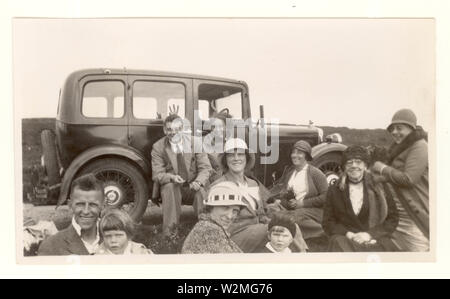 1920 foto di famiglia o amici vestito in abiti smart, tute, cloche cappelli, divertirsi e fare scherzi circa un'escursione accanto a un'auto d'epoca, U.K. Foto Stock