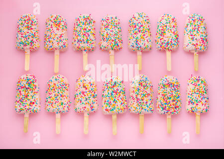 Righe di popsicles con coperte di ghiaccio e spruzza su sfondo rosa Foto Stock
